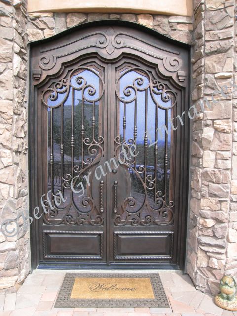 Photo of elegant double iron door w/ twisted tube pull, glass panel. Crafted by Bella Grande Entrances, installed in Las Vegas house.