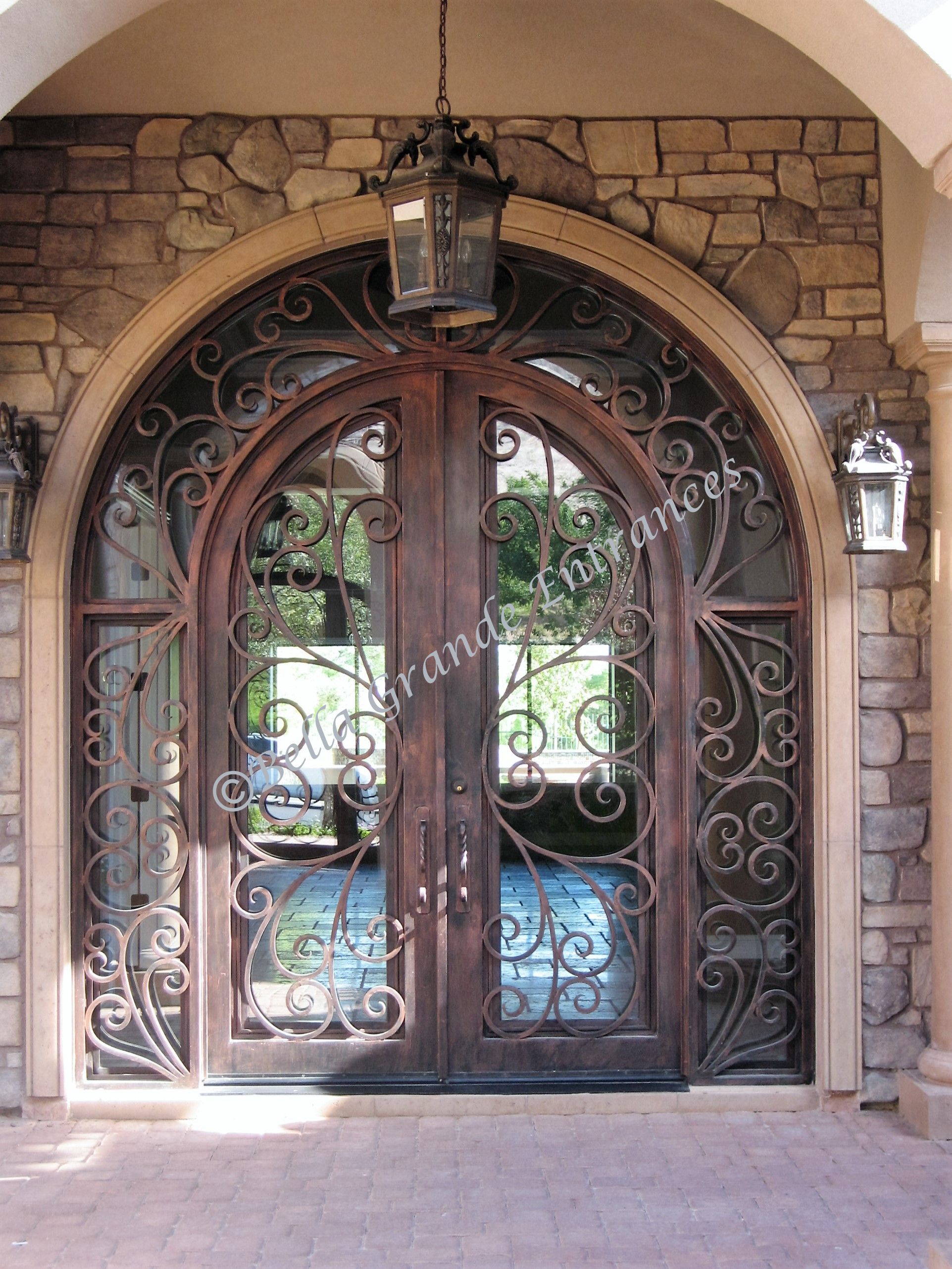 Photo of a luxurious curved ornamental double iron door with iron side and front lights at a brick textured exterior house in Las Vegas, proudly crafted by Bella Grande Entrances.