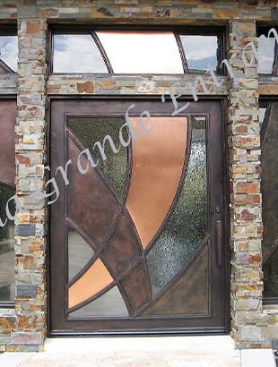 This is a stunning shot of an exquisite contemporary Iron door with a beautiful maximum bronze and medium bronze color. The iron door is located at the entrance of a brick-textured building, adding a touch of elegance and style to the overall design.
