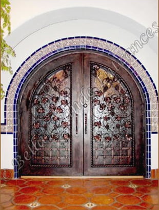 A stunning image captures the intricate details of a gorgeously crafted, Minimum Bronze colored decorative wine and pantry iron doors, adorning a pristine white house. The grand entrance features stunning tiles in vibrant shades of orange, creating an atmosphere of sophisticated elegance.